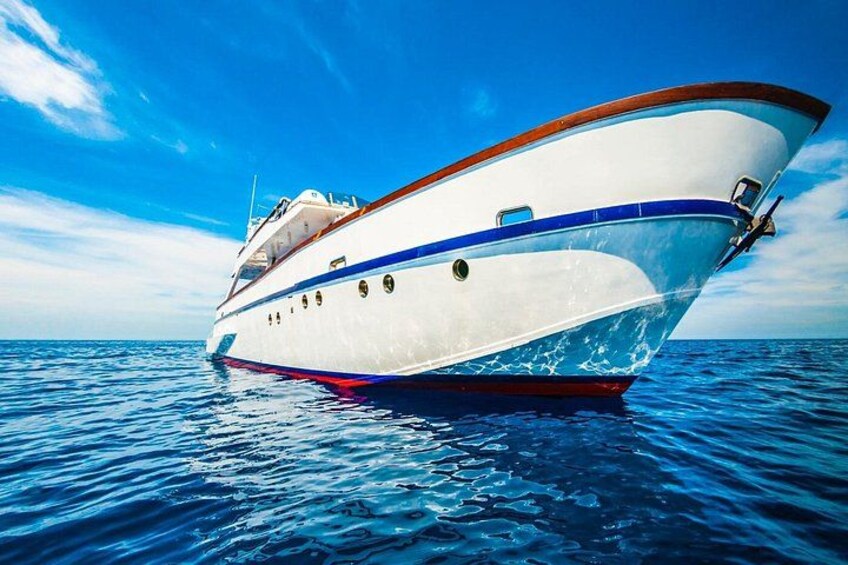 Eine große weiße Yacht mit blauer Zier und rotem Rumpf, die auf ruhigem, blauem Wasser unter einem wolkenlosen Himmel schwimmt. 2