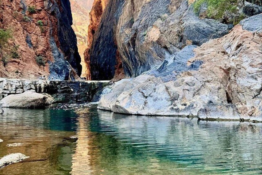 A canyon with a clear water stream, rocky terrain, and a small waterfall. 3