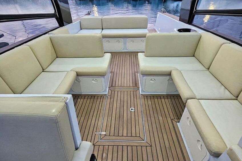 Interior de un barco con asientos acolchados color beige, cubierta de madera y vista al agua a través de amplias ventanas. 3