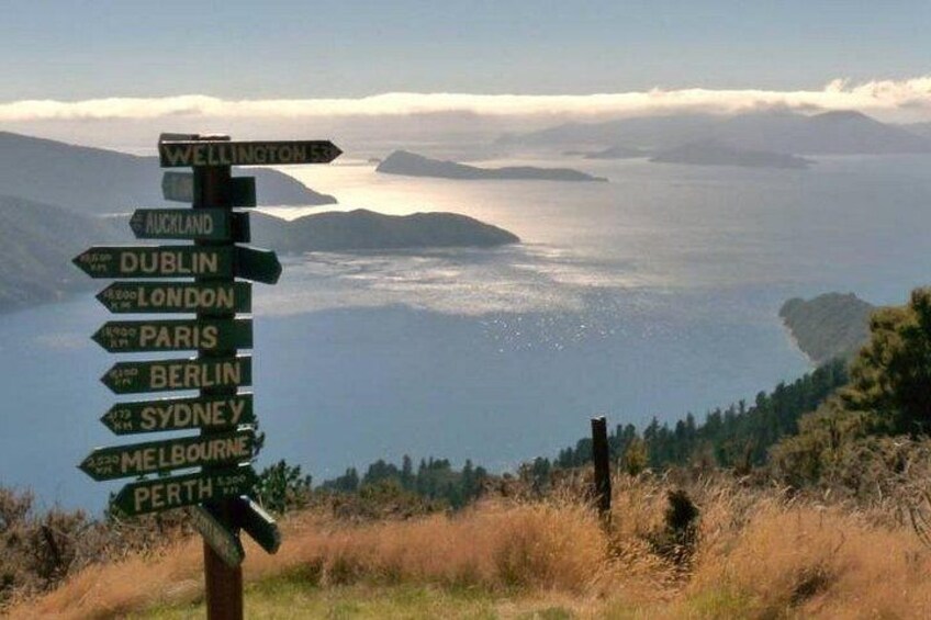 A directional signpost with multiple destination names, overlooking a body of water and distant land. 2