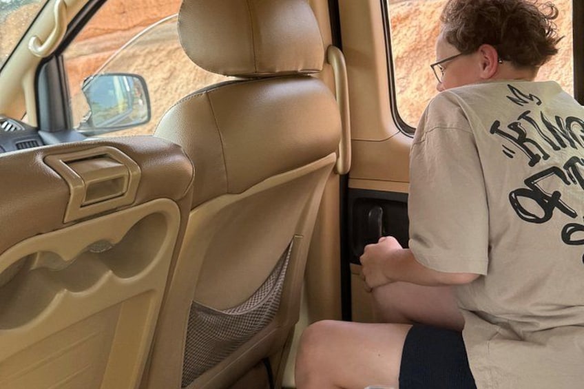 Una persona sentada en el asiento trasero de un coche, con una camisa color beige con texto en la parte posterior. 2