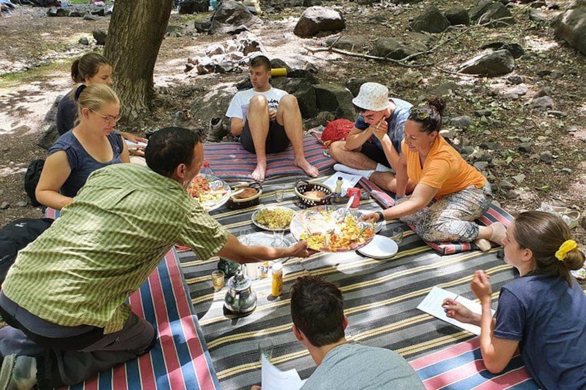 Un grupo de personas sentadas sobre una manta a rayas al aire libre, comiendo y conversando. 4