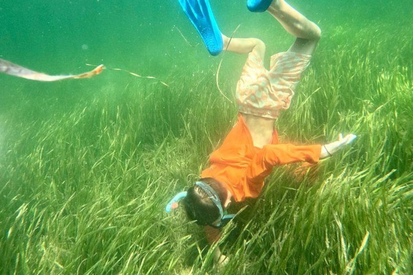 A person submerged in water, wearing orange swimwear and a blue swim cap, lying on their back with a blue flotation device. 4