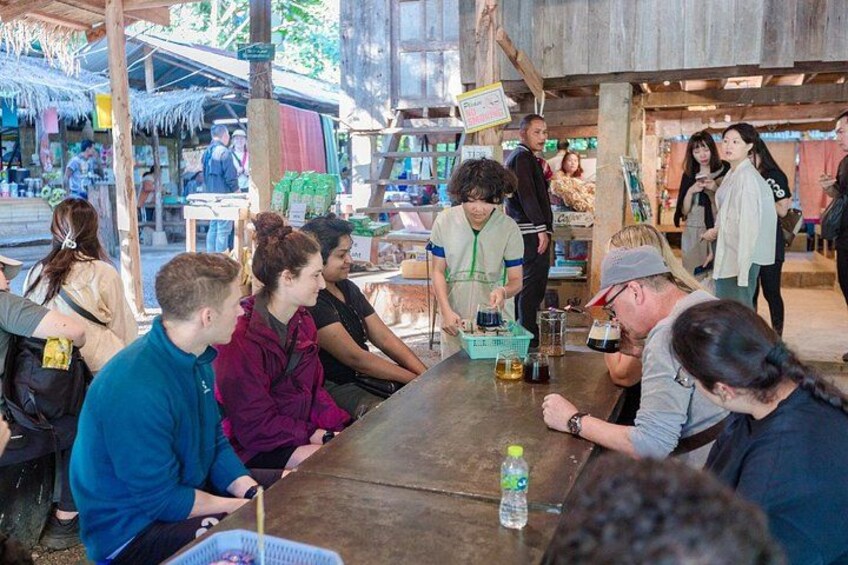 A group of people sitting around a wooden table at an outdoor market. 5
