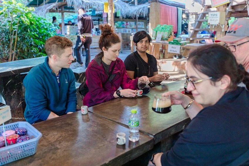 A group of people sitting at a wooden table in a casual setting, possibly a cafe or restaurant. 3