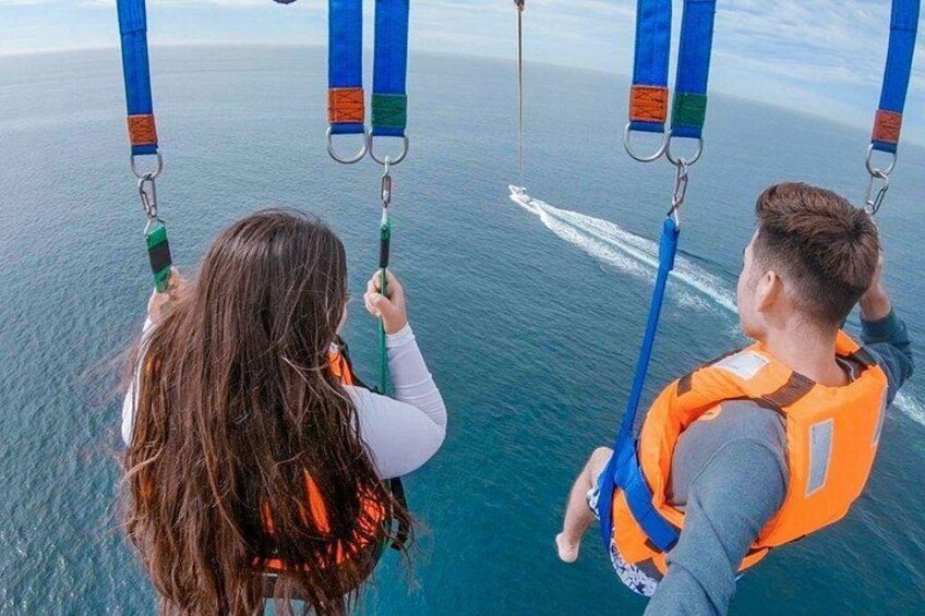 Two people on a boat, wearing life jackets, holding onto blue straps. 2
