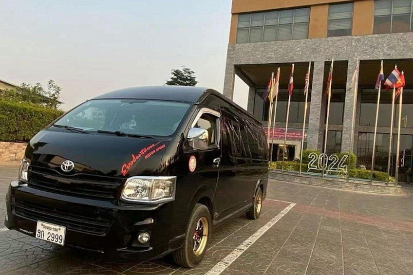 A black Toyota Hiace van parked in front of a building with flags and the year 2024 displayed. 4
