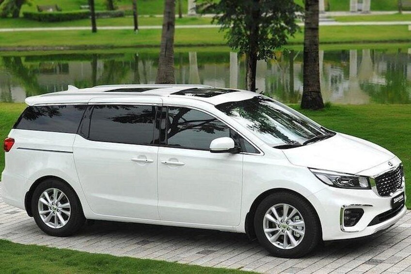 A white minivan parked on a paved area with a grassy field and a body of water in the background. 5