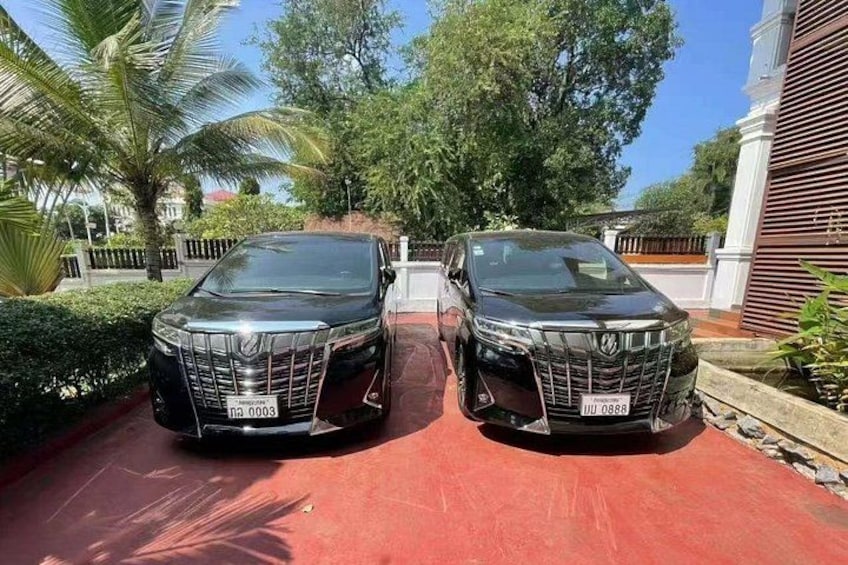 Two black cars parked on a red surface with trees and a building in the background. 2
