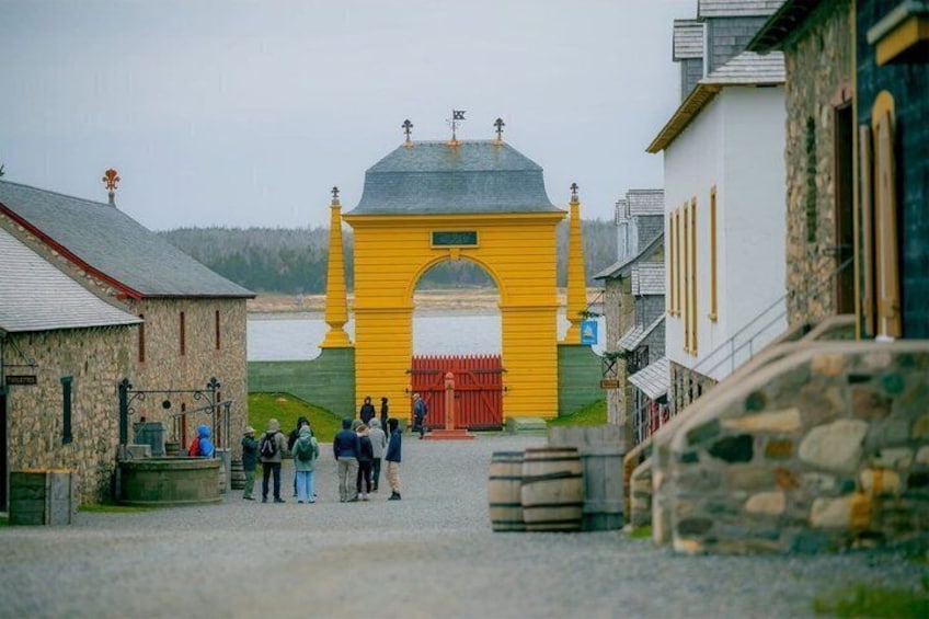 Un arco amarillo con un portón rojo, rodeado de edificios de piedra y una masa de agua al fondo. 5