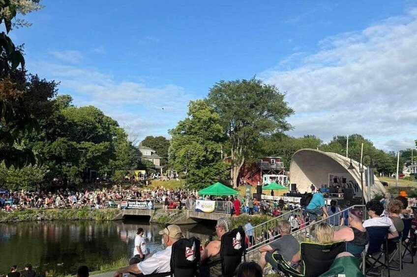 A riverside gathering with people, a stage, and a bridge. 4