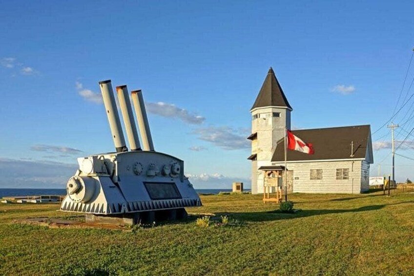 A large cannon, a church with a tower, and a grassy field. 1