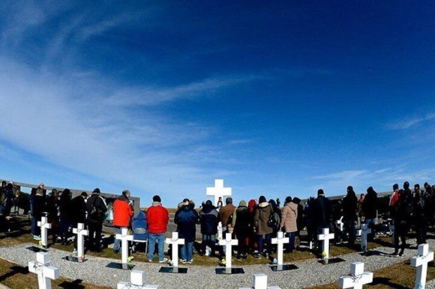 Un grupo de personas reunidas alrededor de una fila de cruces blancas en un campo abierto. 4