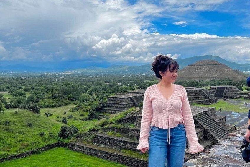 A person standing on a stone platform overlooking ancient ruins with a mountainous landscape in the background. 3