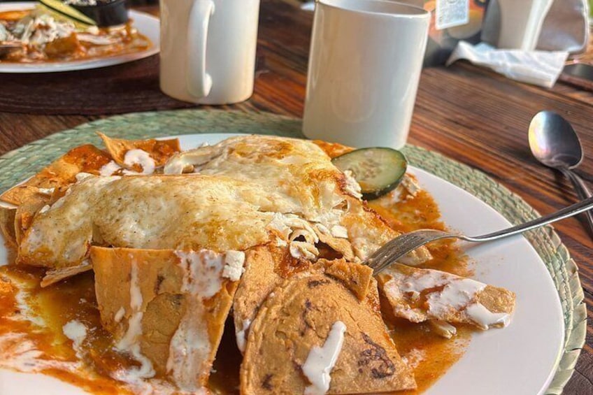 A plate of enchiladas with melted cheese and sauce, a fork, and a spoon on a table. 5