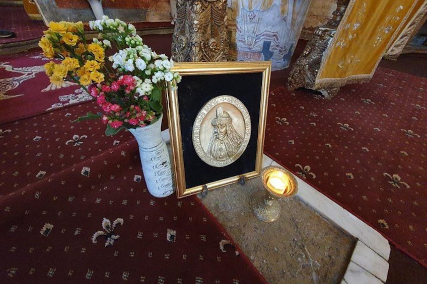 A framed religious icon with a lit candle, a vase of flowers, and a patterned carpet. 1