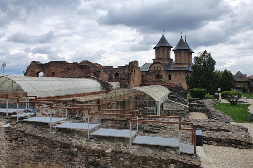An ancient ruin with a church in the background, a greenhouse, and a paved walkway. 4