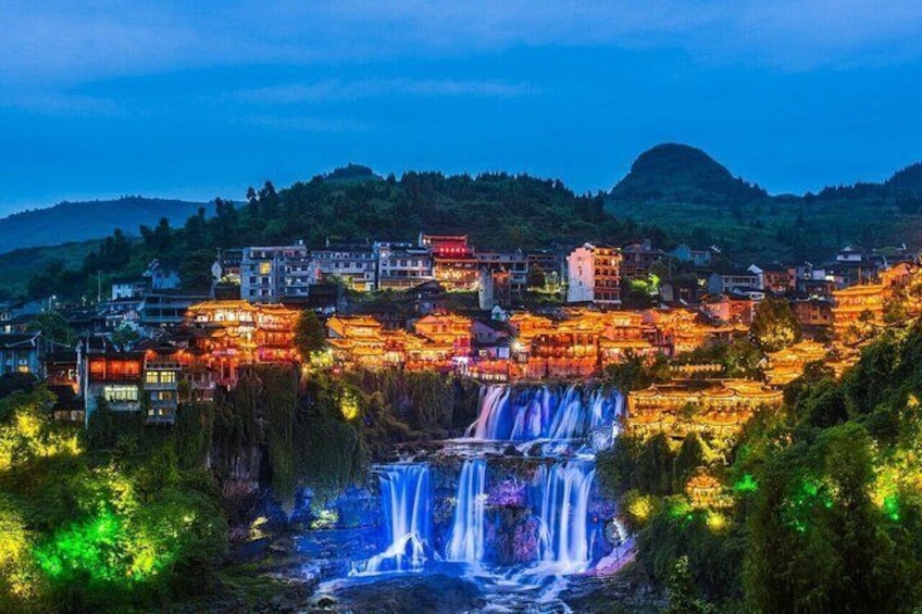 A town with illuminated buildings and a waterfall. 1