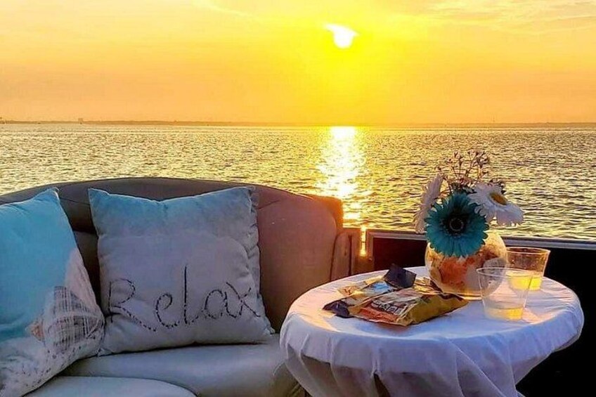 Ein Sonnenuntergang über dem Meer, ein weißer Tisch mit einem Getränk und ein Sofa mit Kissen. 1