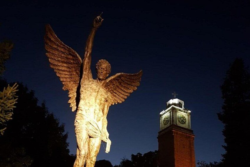 Una estatua de un ángel con alas extendidas, una torre del reloj y un cielo nocturno despejado. 3