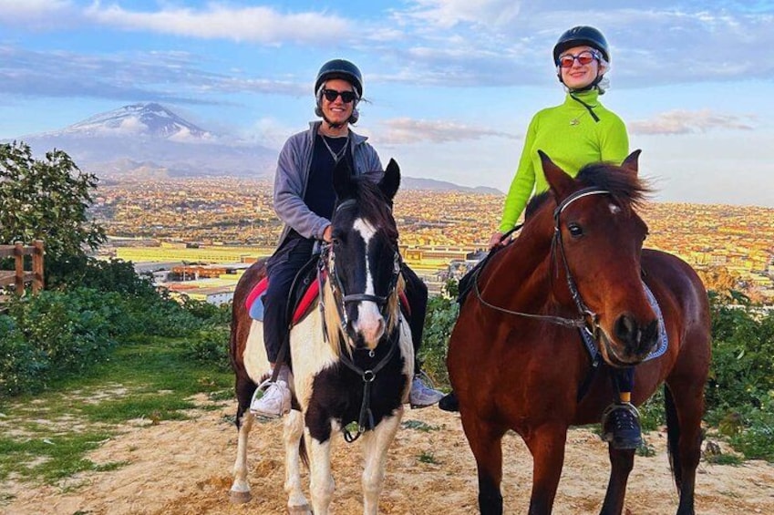 Dos personas montando a caballo por un sendero de tierra, con una ciudad y una montaña al fondo. 1