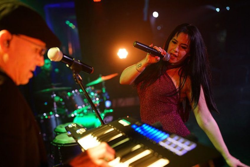 A person playing a keyboard and singing into a microphone on stage. 5