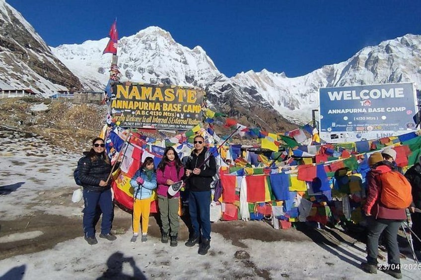 A group of people at the Namaste Annapurna Base Camp with a signboard and prayer flags. 1