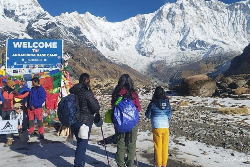 A group of hikers at the Annapurna Base Camp sign with snow-covered mountains in the background. 4