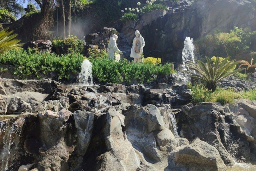 A rocky landscape with a waterfall, statues, and lush greenery. 4
