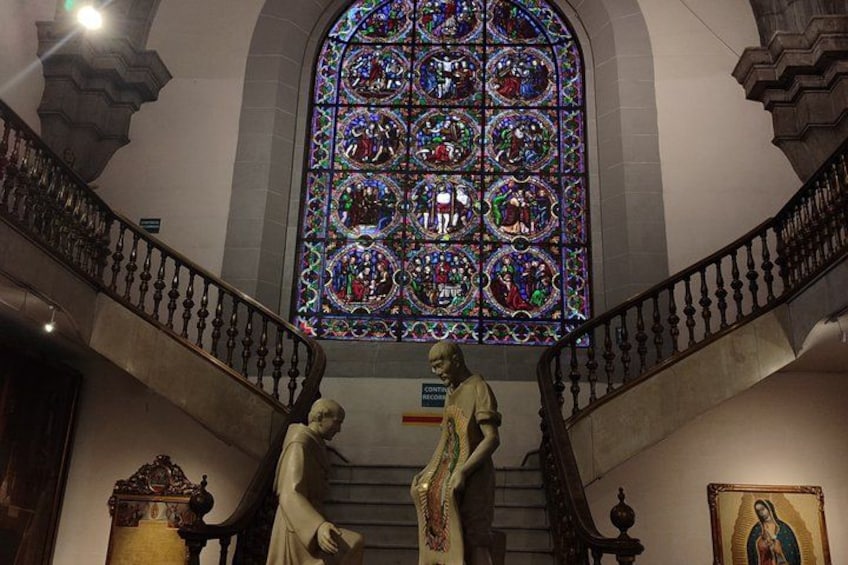 A stained glass window, a statue, and a staircase in a building. 2