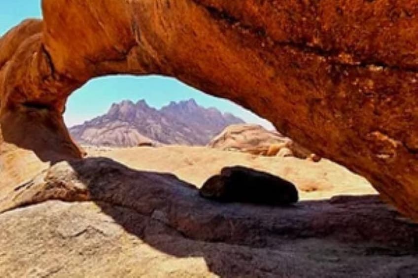 Une formation rocheuse dotée d’une arche naturelle, un paysage désertique et des montagnes à l’horizon. 1