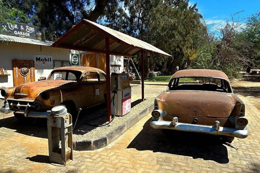 Dos autos antiguos estacionados en una gasolinera, con un edificio identificado como 'Mobil' al fondo. 4
