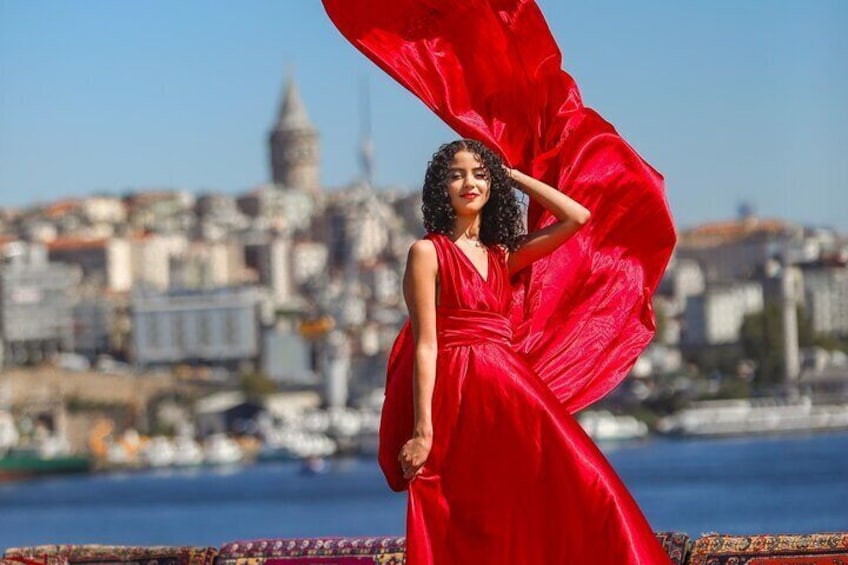 Una persona con un vestido rojo parada junto a la costa, con un paisaje urbano al fondo. 1