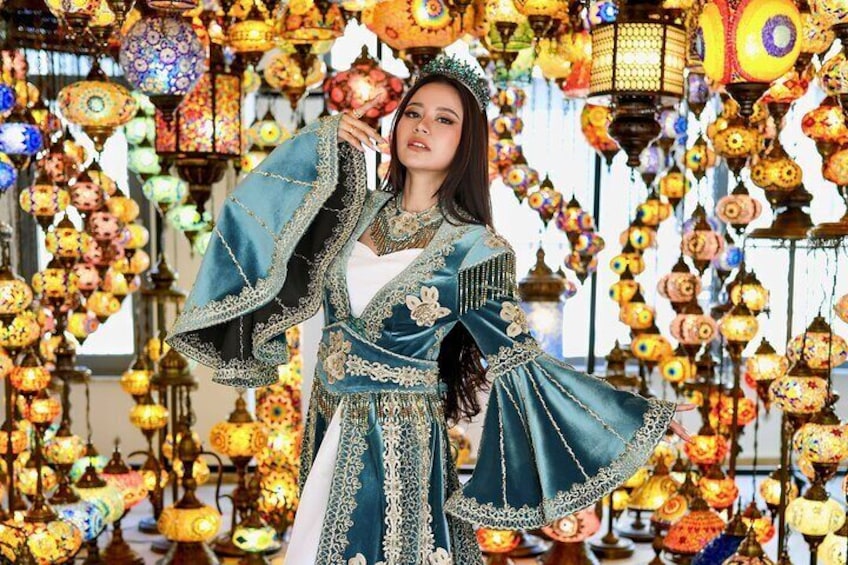 Una persona vestida con atuendo tradicional y bordados elaborados, rodeada de lámparas decorativas colgantes. 2