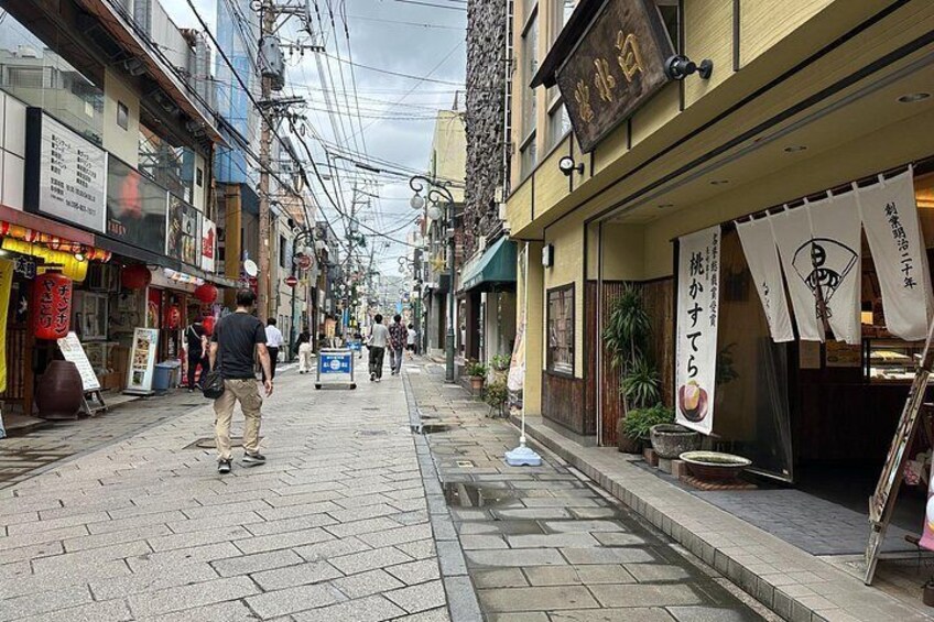 A narrow urban street with shops and pedestrians. 3