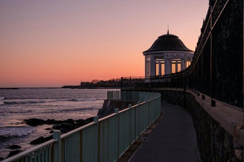A coastal walkway with a gazebo and a sunset in the background. 3