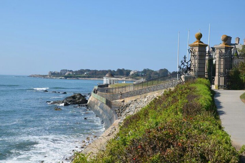A coastal promenade with a stone wall, a pathway, and a building with domed roofs. 5