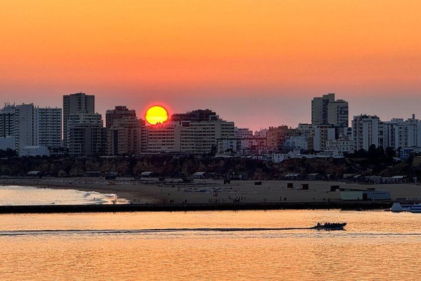 Un atardecer sobre el horizonte de una ciudad con edificios, una playa y un barco en el agua. 1