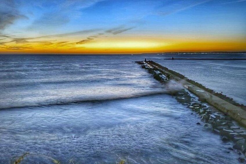 Escena costera con olas, un rompeolas y una puesta de sol. 5
