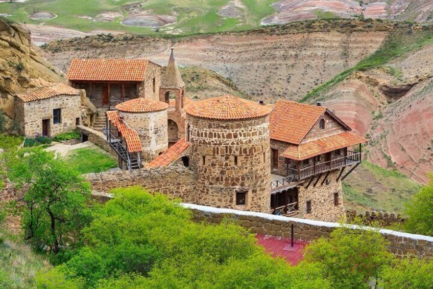 Un château de pierre coiffé d’un toit de tuiles rouges, entouré d’une végétation luxuriante et d’un paysage accidenté. 3