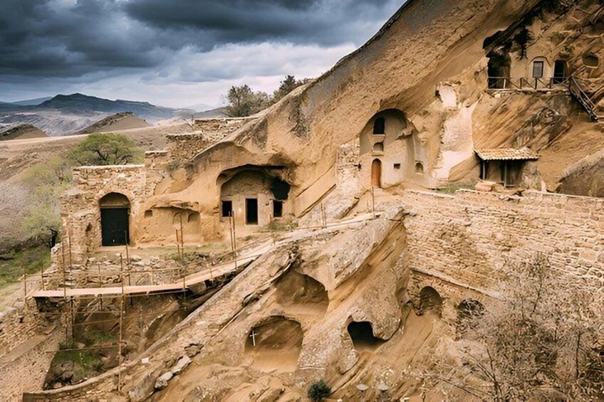A rugged landscape with ancient rock-cut architecture, including a staircase leading to a small building with arched openings. 3