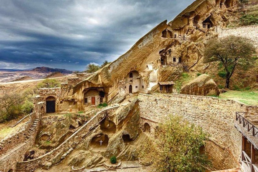 A rock-cut architecture with multiple dwellings carved into the hillside, a stone staircase, and a cross symbol. 4