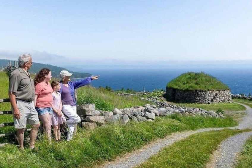 A family standing on a grassy hill overlooking a stone structure with a view of the ocean. 1