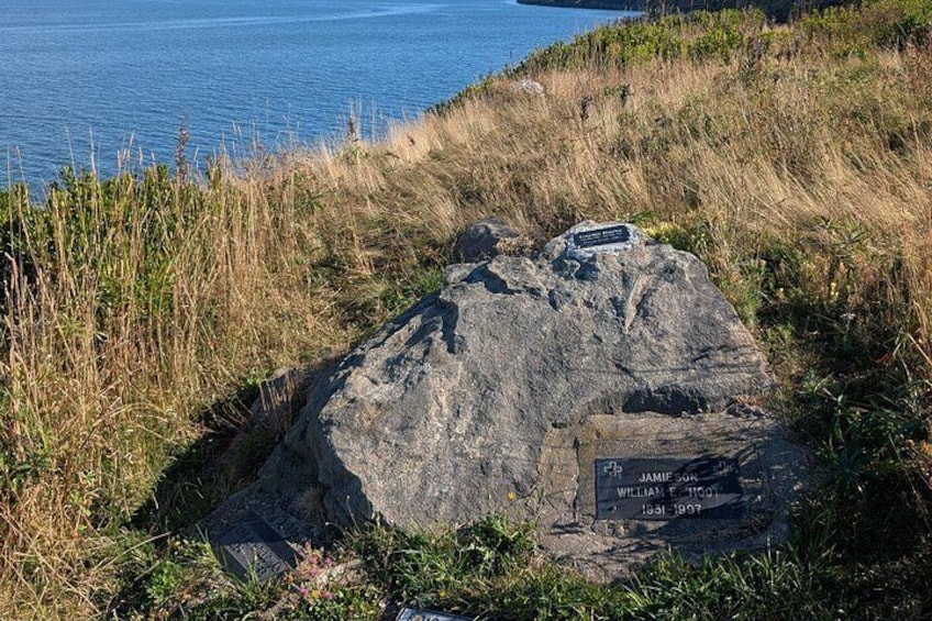 A large rock with a plaque, surrounded by grass and overlooking a body of water. 4