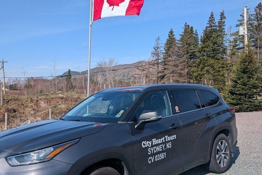 A black SUV with 'City Heart Tours Sydney, NSW CV 03561' on the side parked in front of a Canadian flag. 2