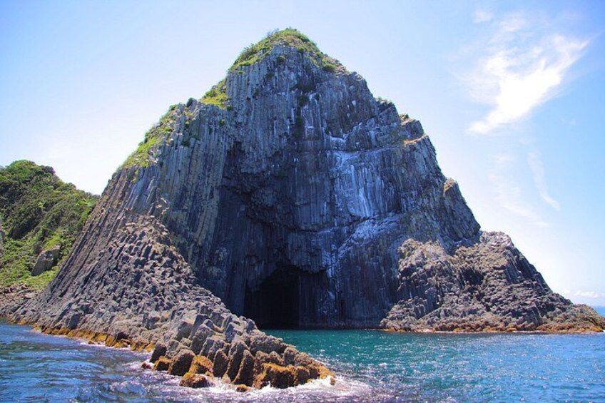 A large rock formation with a cave entrance surrounded by turquoise water and green vegetation. 3