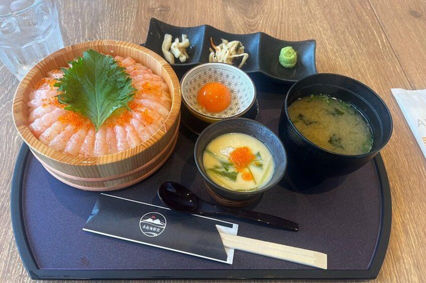 A wooden bowl of sashimi with a leaf garnish, a small bowl of wasabi, a bowl of soup, and a small dish of pickled ginger. 2