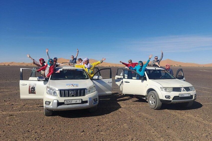 Two off-road vehicles parked in a desert with people standing on them. 2