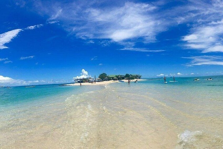 A beach with clear turquoise water, a sandy shore, and a small island with buildings in the distance. 3