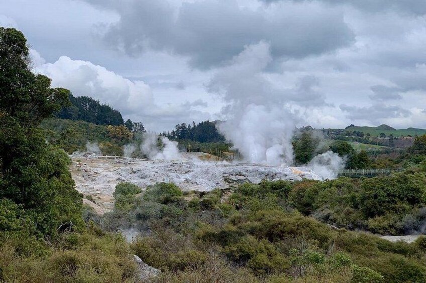 A geothermal area with steam vents, surrounded by greenery and hills. 4